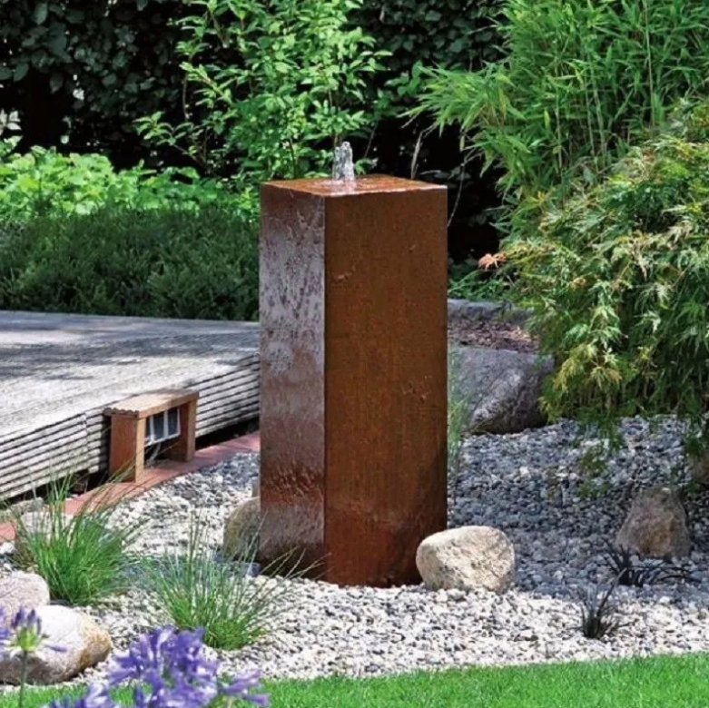 Modern metal fountain a with bubbler on top in a green garden setting
